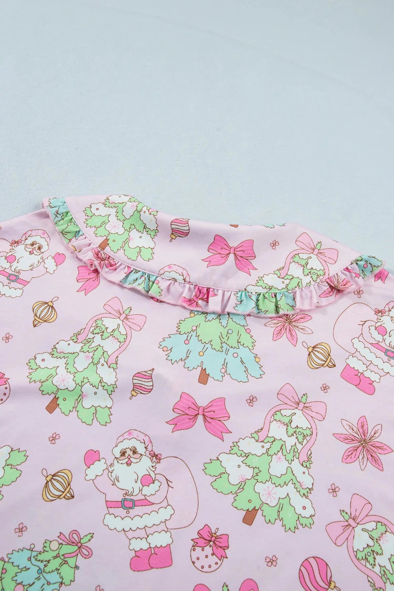 Close-up of pink holiday garment with Santa, trees, bows, ornaments, and ruffled collar.