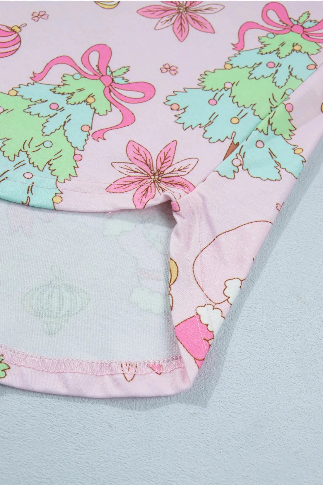 Close-up of light pink fabric with green trees, pink bows, and gold details.