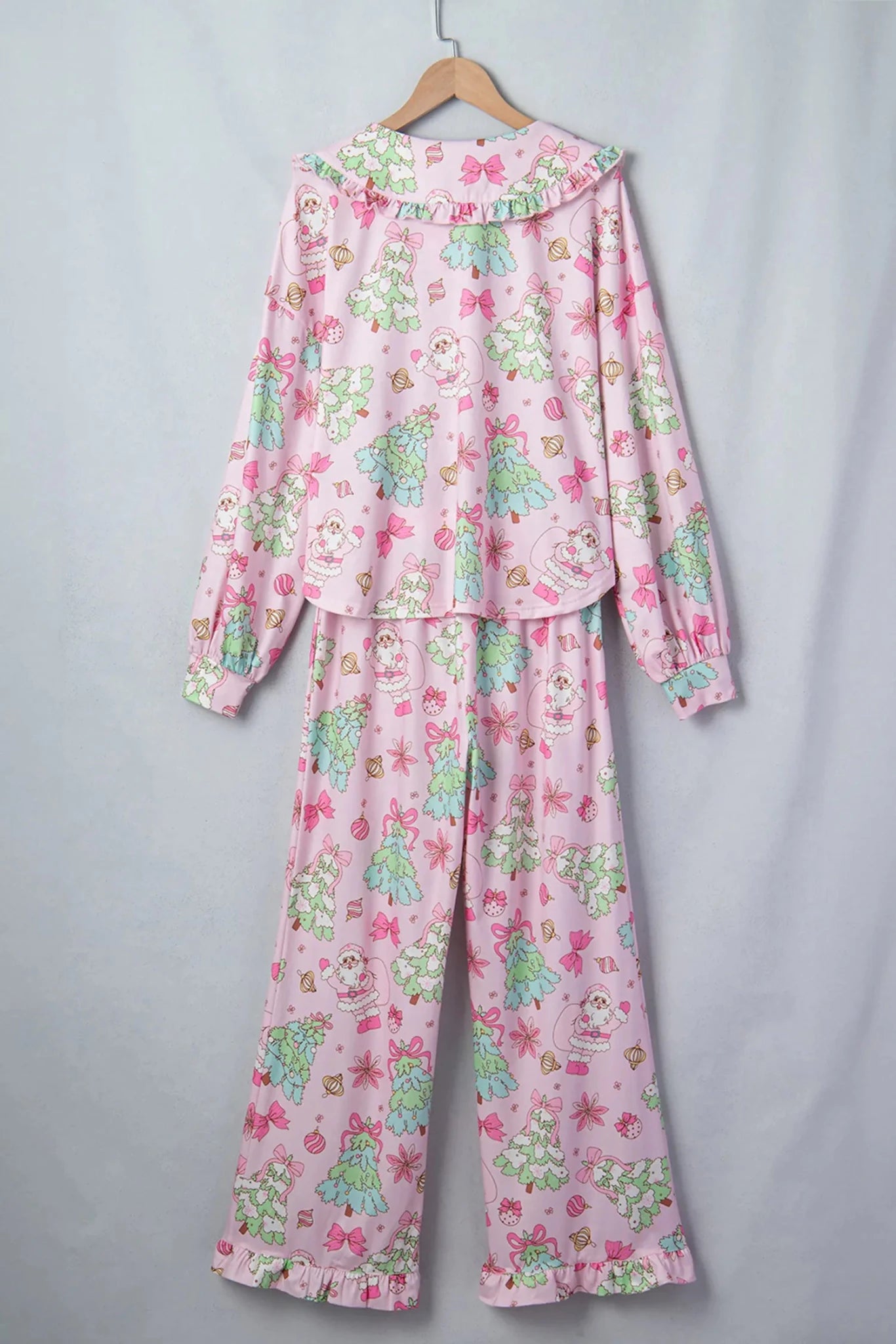 Light pink pajamas with Christmas trees, red bows, and Santa print on hanger.