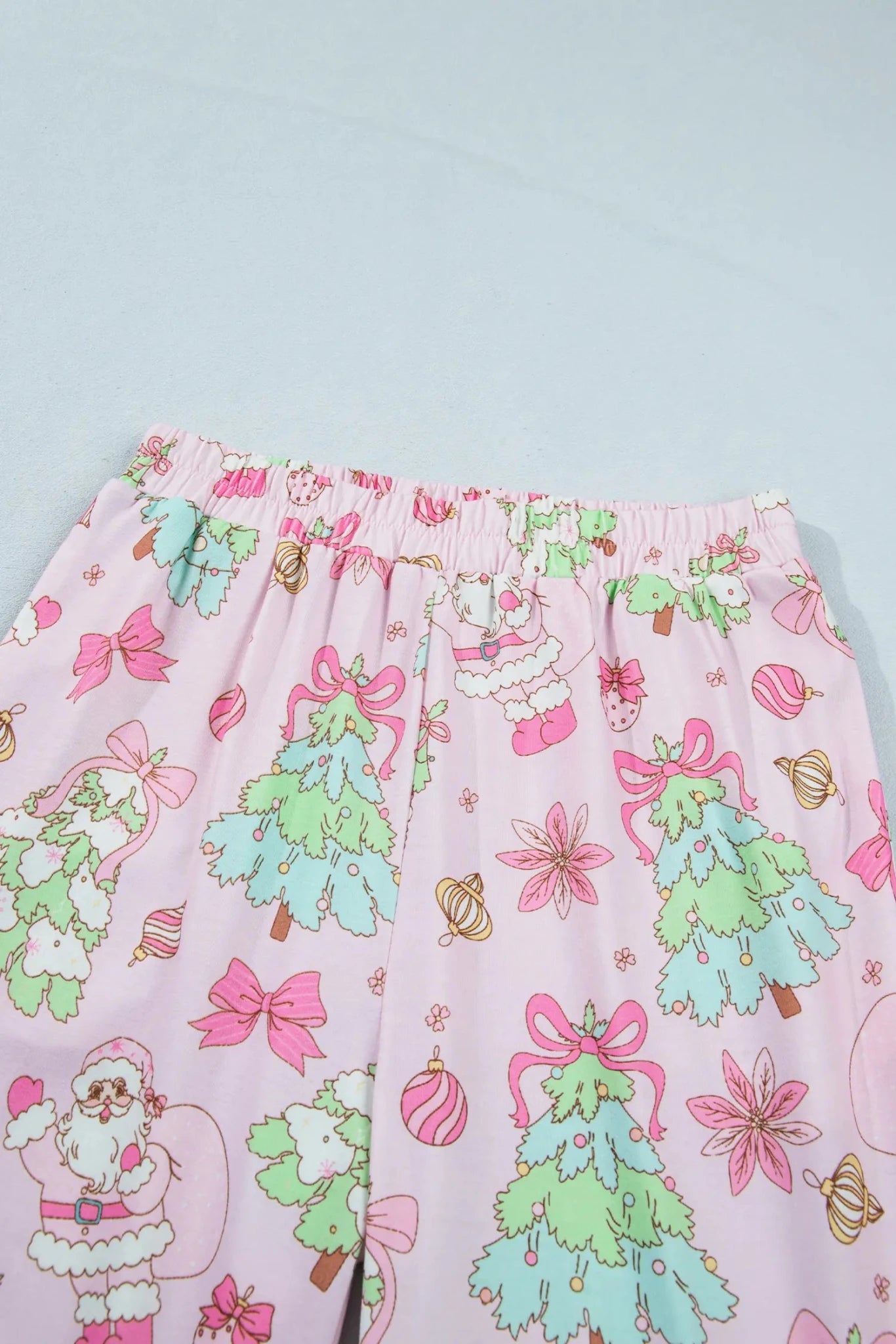 Pink pajama pants with Santa, trees, bows, and ornaments print.