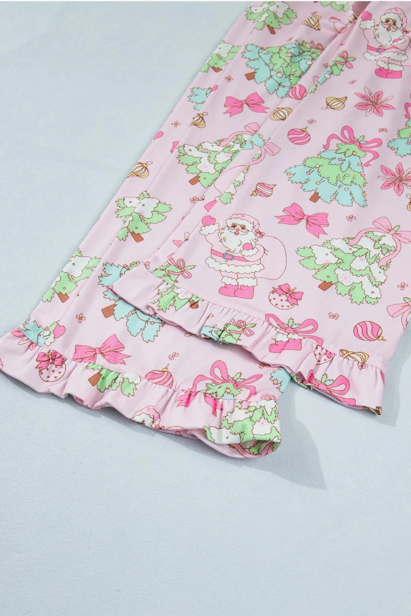 Pink pajama pants with festive Christmas print, laid flat on a light blue-gray background.