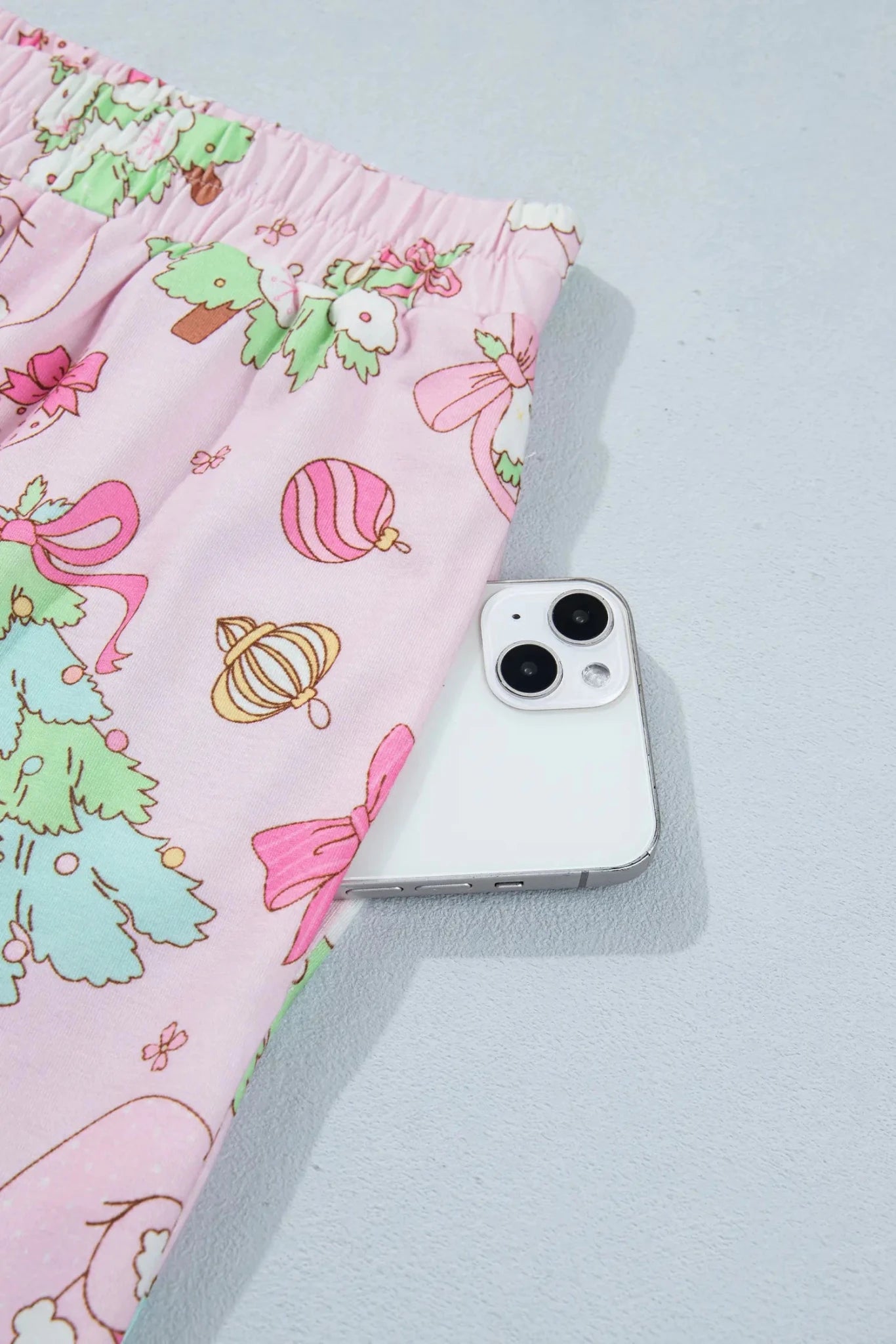 Close-up of pink fabric with festive Christmas tree, ornaments, and bows print.