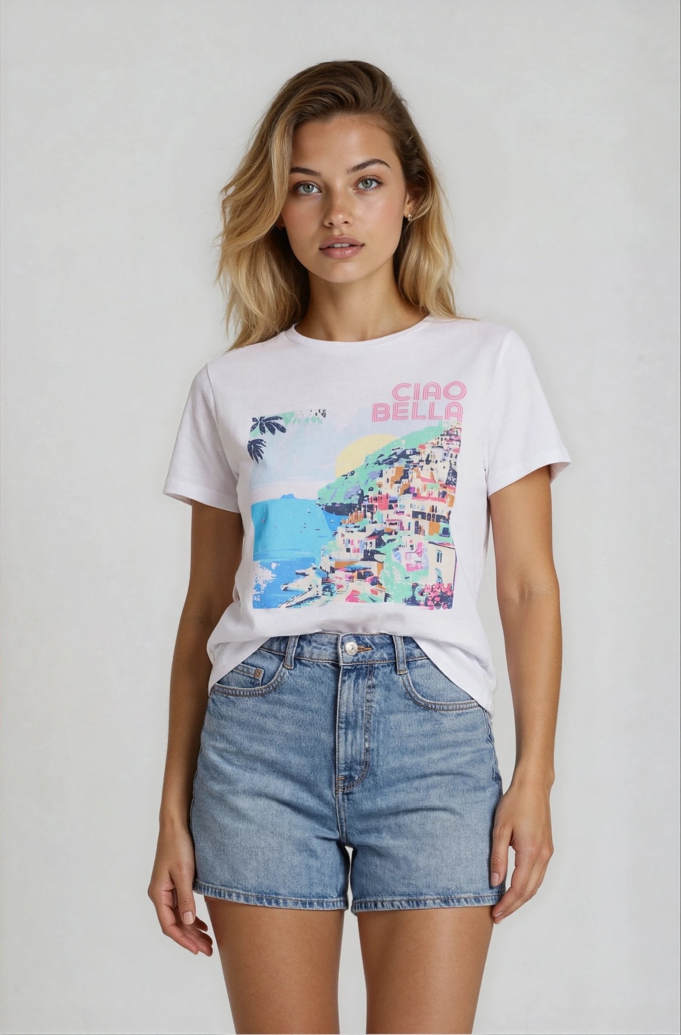 Woman wearing a white t-shirt with colorful graphic and 'Ciao Bella' text, paired with denim shorts on a plain background.