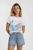 Woman wearing a white t-shirt with colorful graphics and text, paired with denim shorts on a plain background