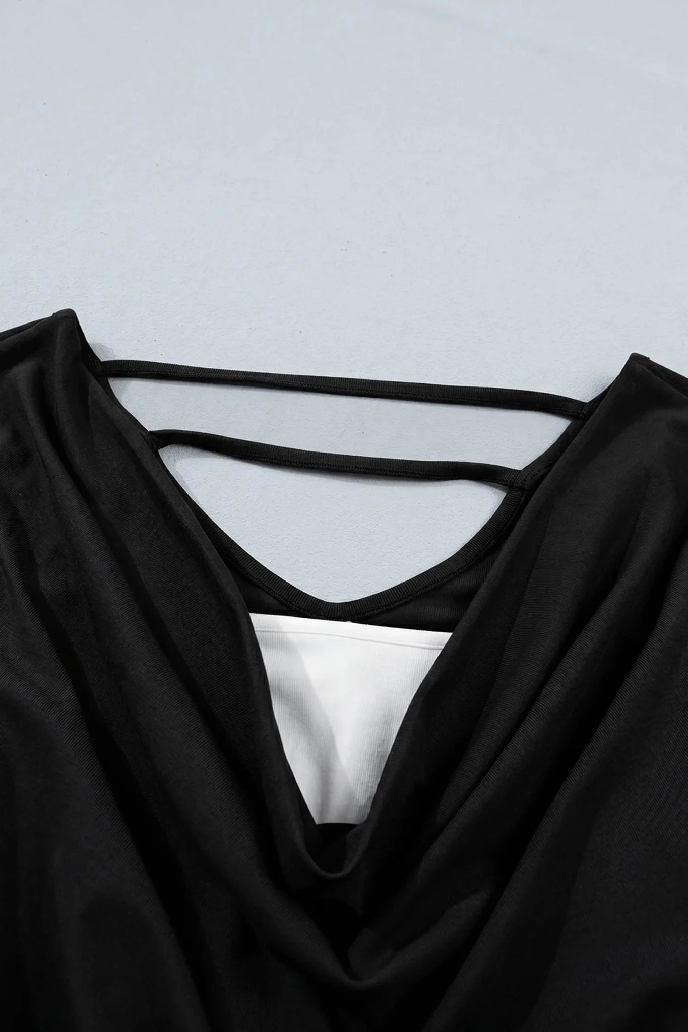 Close-up of black draped top with double straps and white inner layer.
