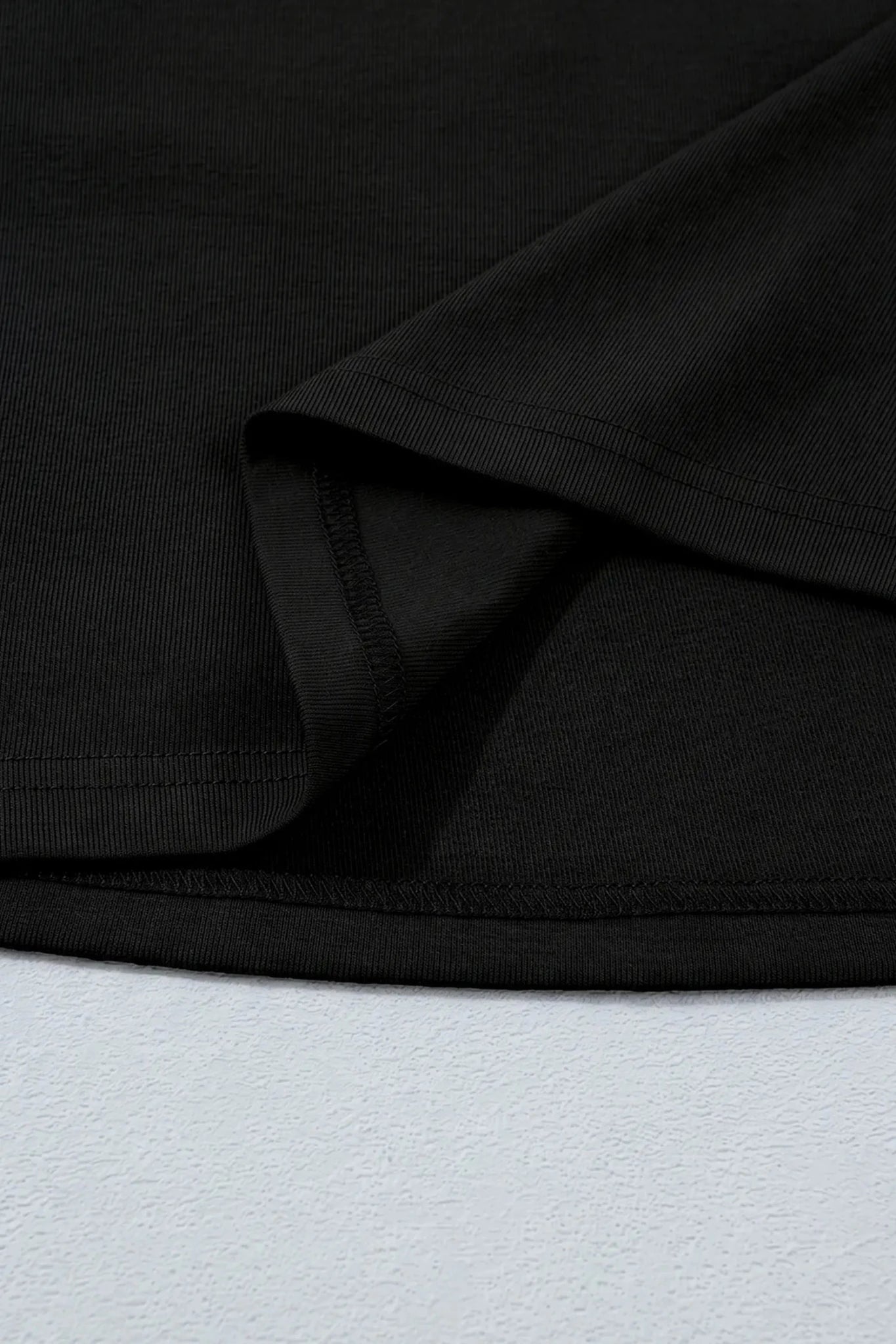 Close-up of black ribbed fabric with textured hem detail.