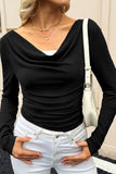 Woman in black cowl-neck top, white jeans, layered gold necklaces, and white bag.