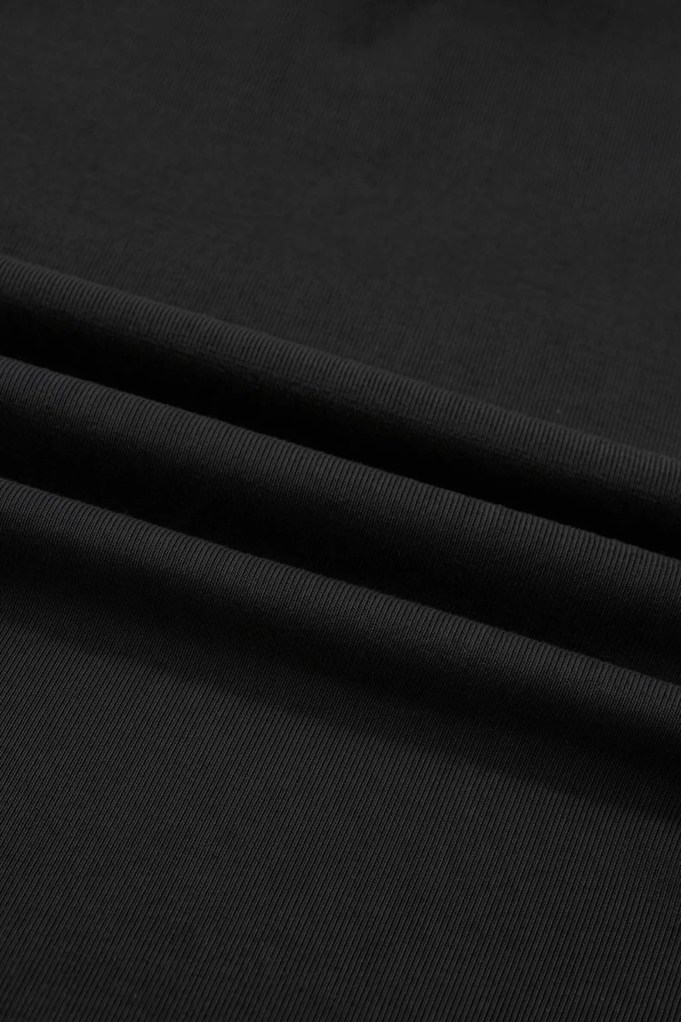 A close-up of black ribbed fabric with soft diagonal folds and a smooth texture.