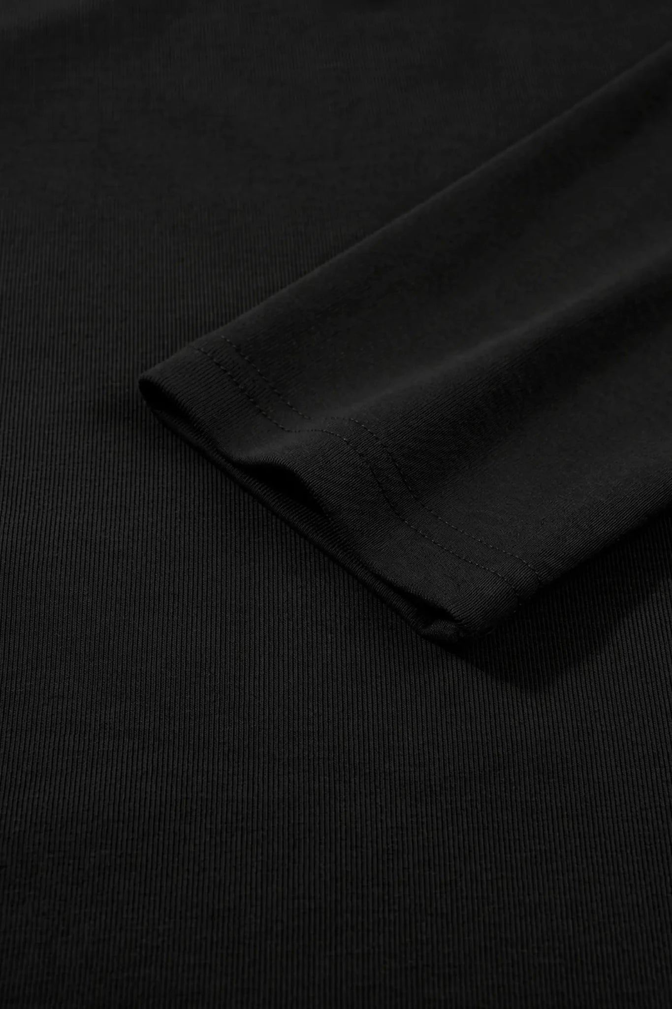 Close-up of a black ribbed knit fabric with a folded cuff showing fine stitching.