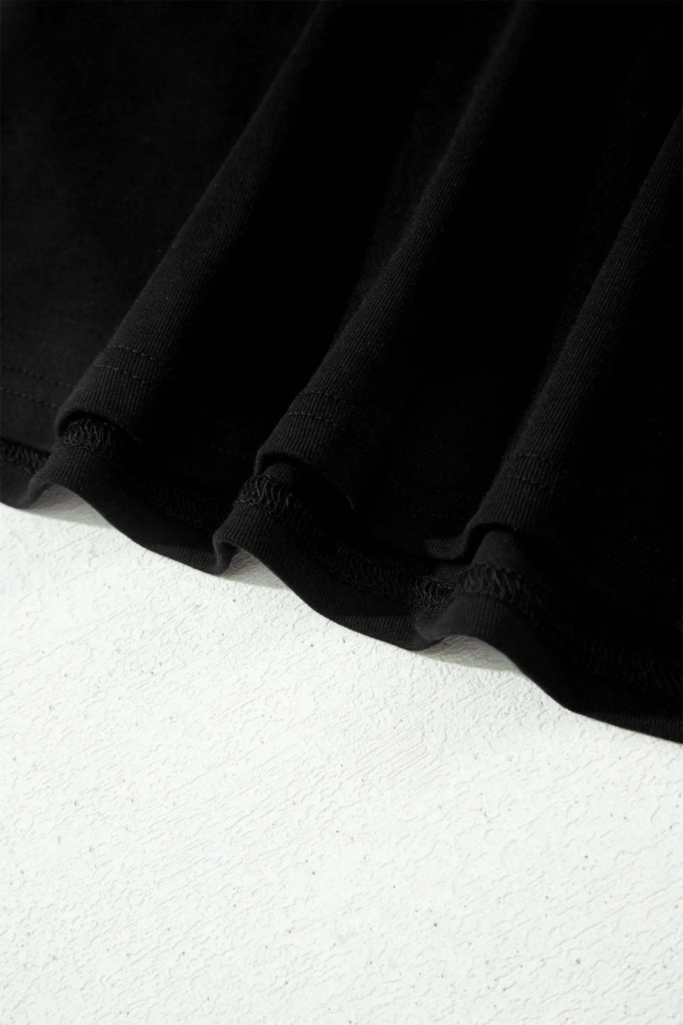 Close-up of black fabric with soft folds and hem detail on white background.