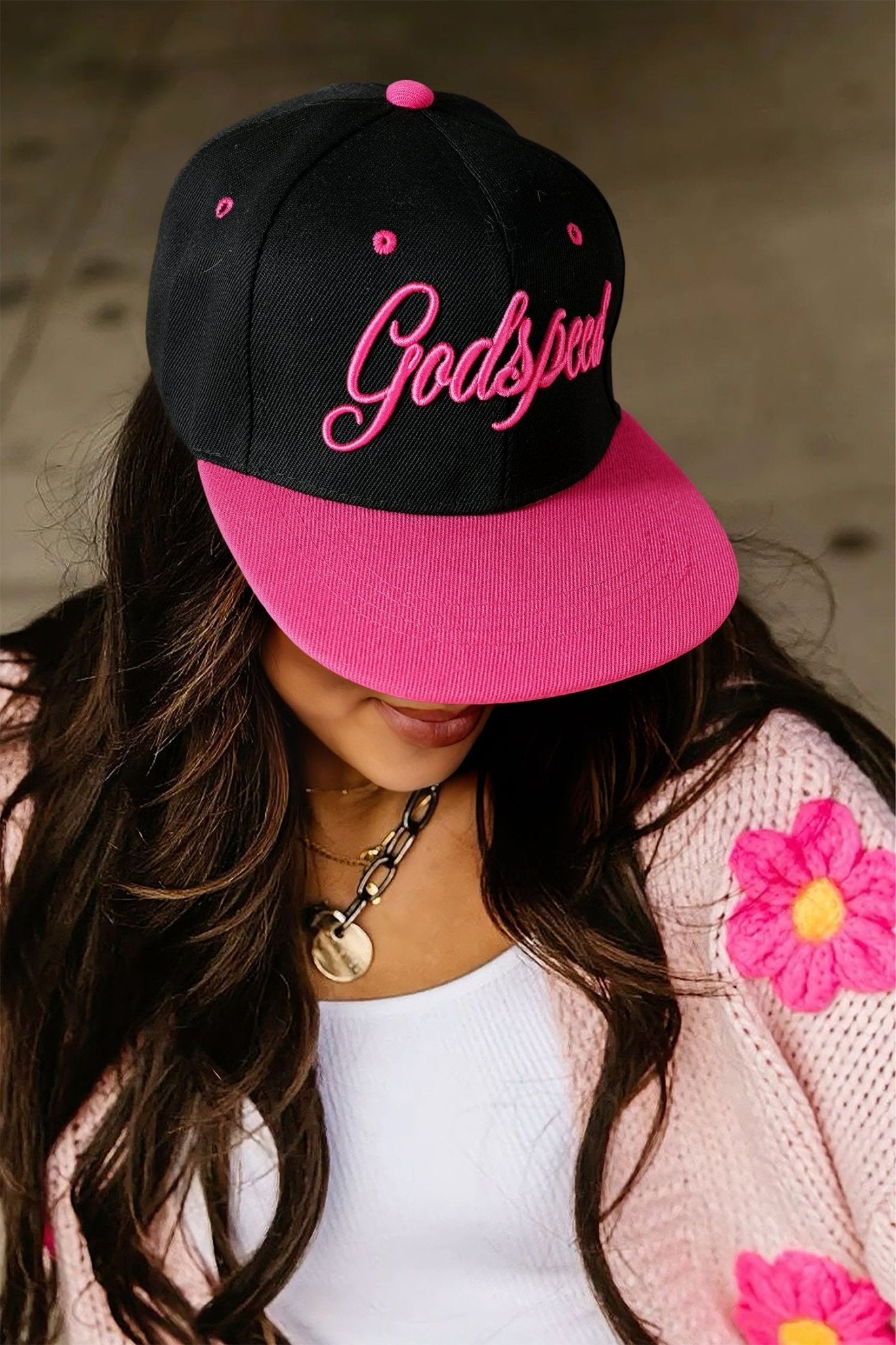 Person wearing a black and pink cap with 'Godspeed' text, surrounded by floral decorations.