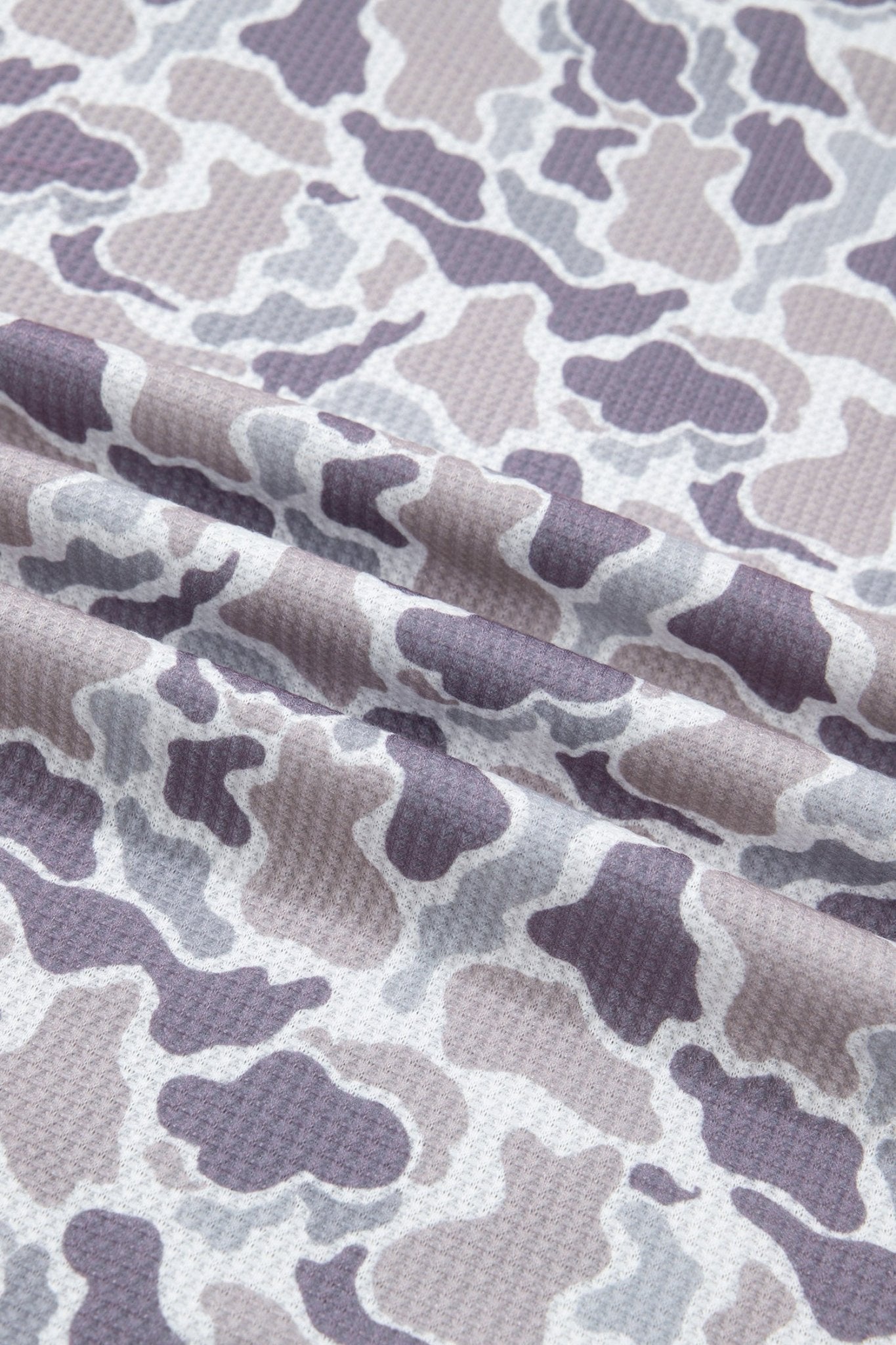 A close-up of draped fabric with an allover camouflage pattern in muted dusty purple, taupe, and off-white.
