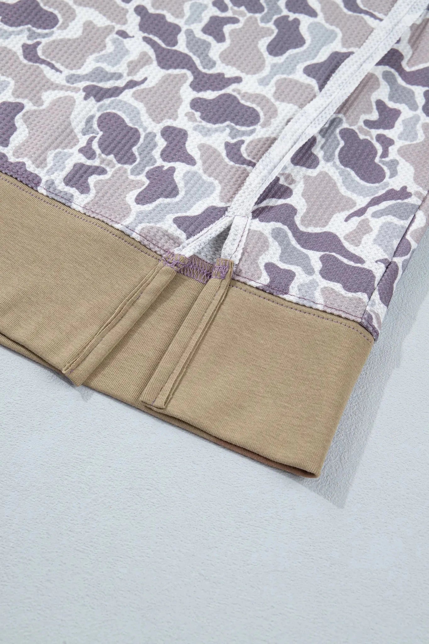 Close-up of beige ribbed cuff, white drawstring, and gray-lavender camo fabric.