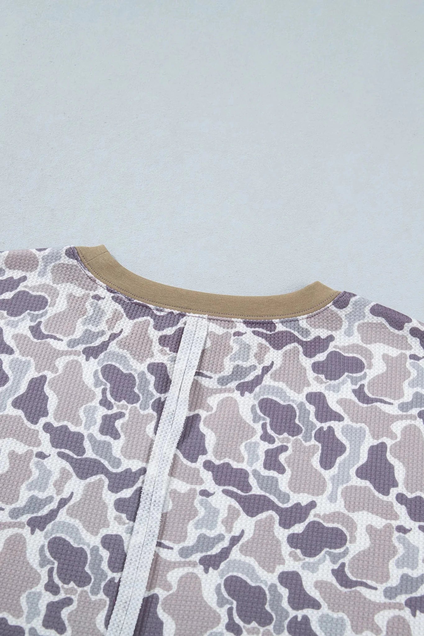 Close-up of beige ribbed collar with white tie and purple-gray camo pattern.

