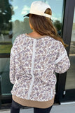 Back view of woman in taupe-white abstract zip jacket, black leggings, and white cap.