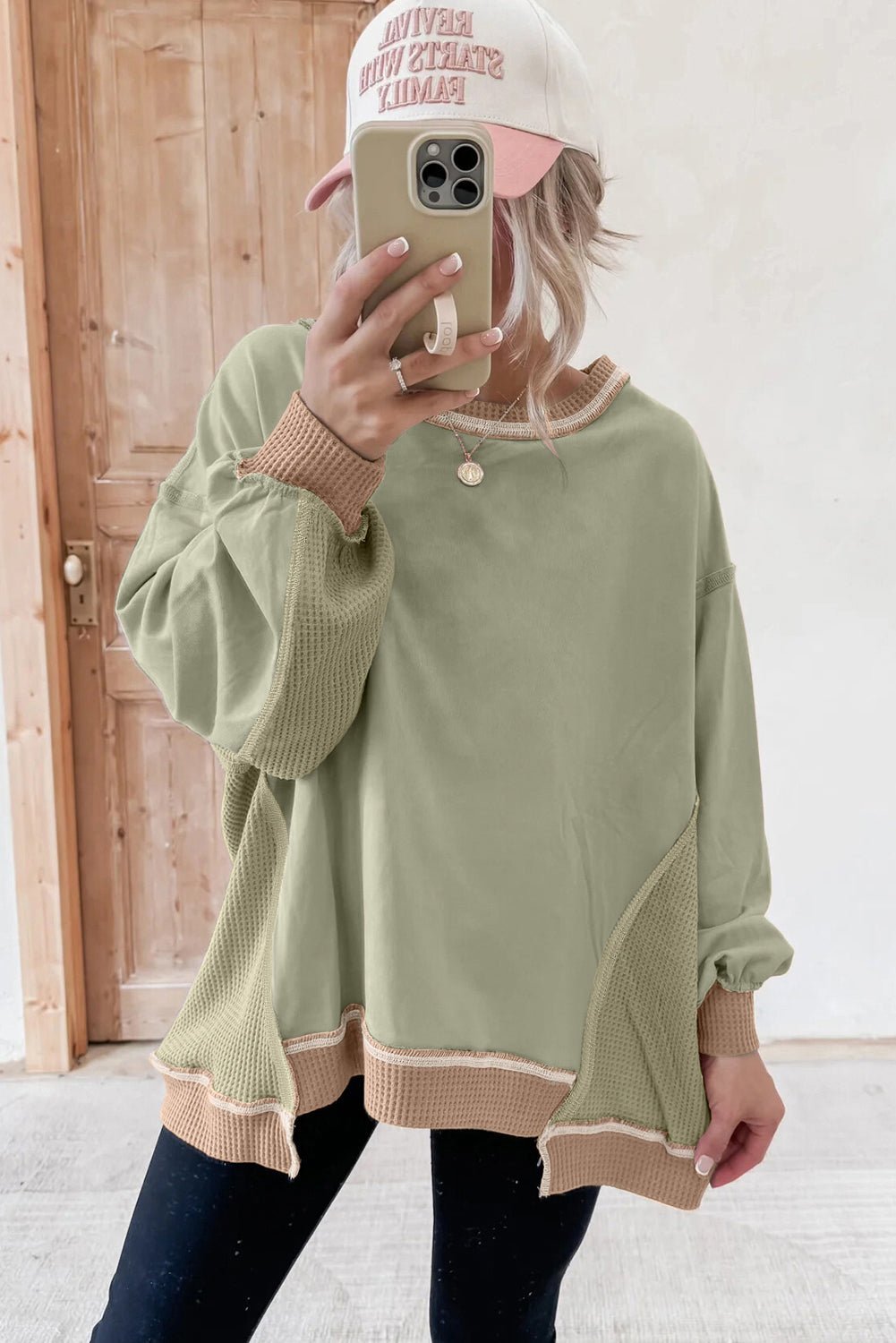 Person wearing a green sweater with checkered cuffs and hem, taking a mirror selfie.