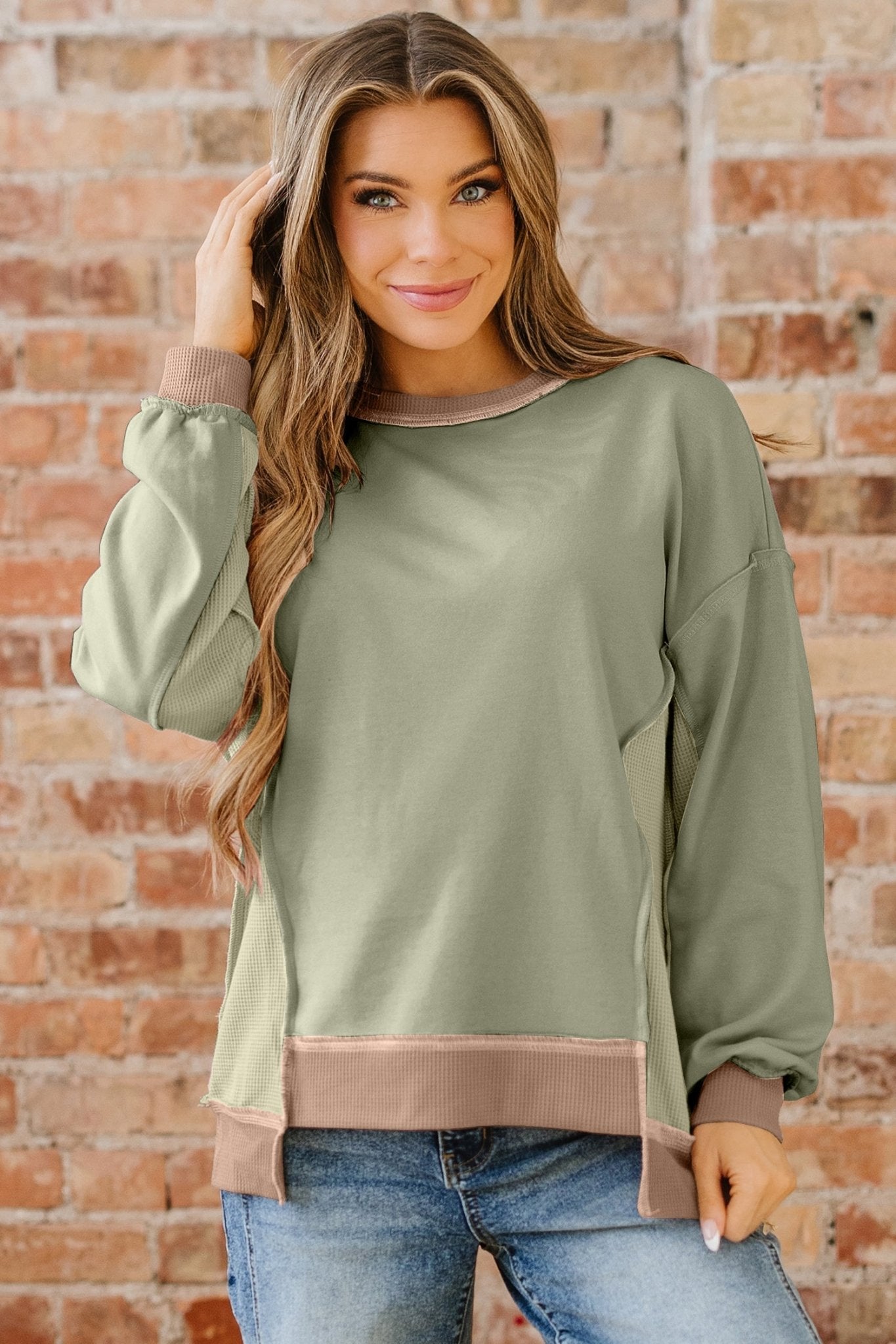Woman wearing a green sweater with brown trim against a brick wall