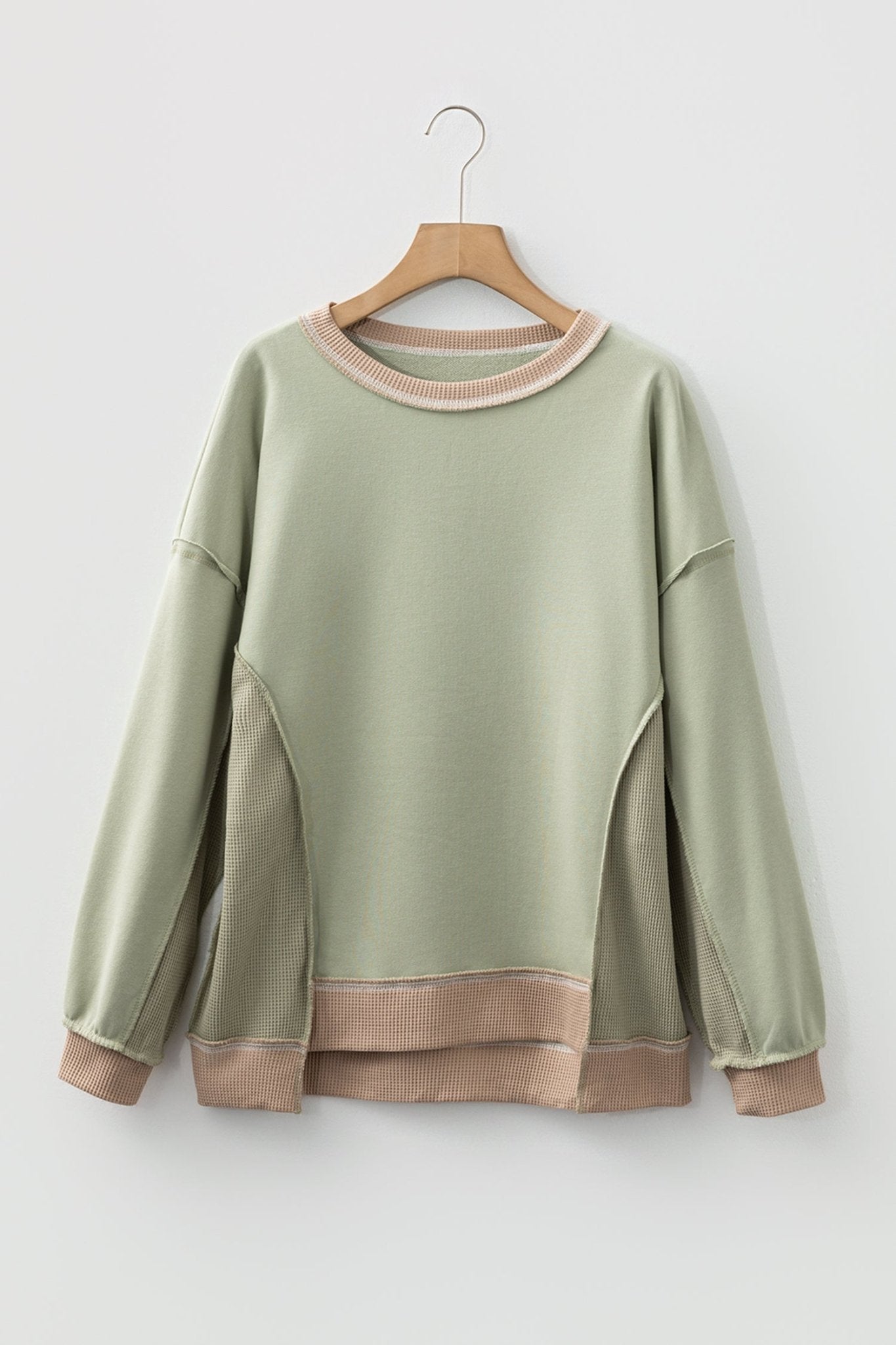 Green sweatshirt with brown trim on a wooden hanger against a white background
