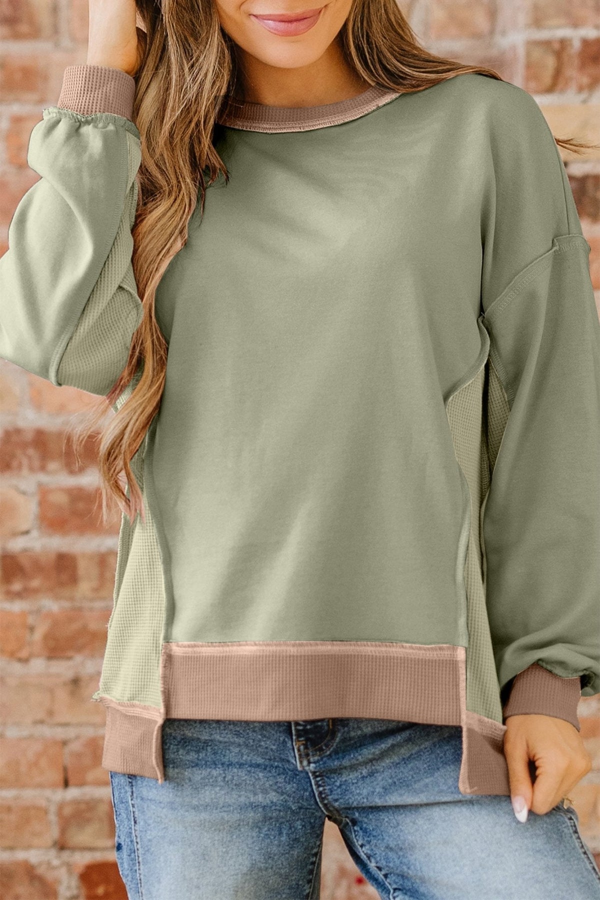 Person wearing a green sweater with brown trim against a brick wall.