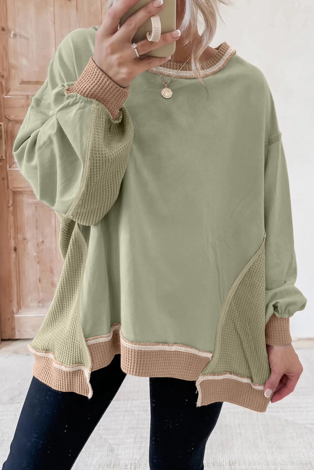 Person wearing a green sweater with beige trim, taking a mirror selfie.