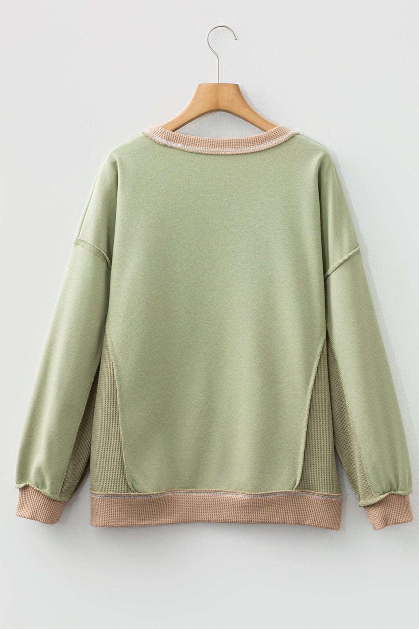 Green sweatshirt on a wooden hanger against a white background