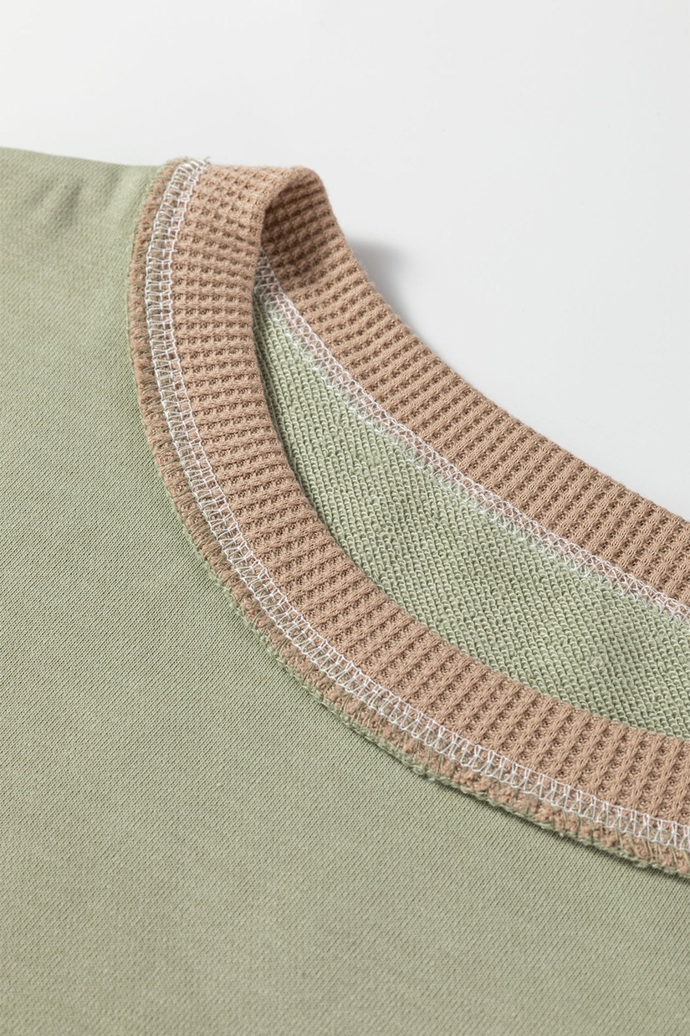 Close-up of a green garment with a textured brown neckline on a white background
