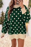 Woman in oversized green polka-dot sweater with cream trim by Christmas tree.