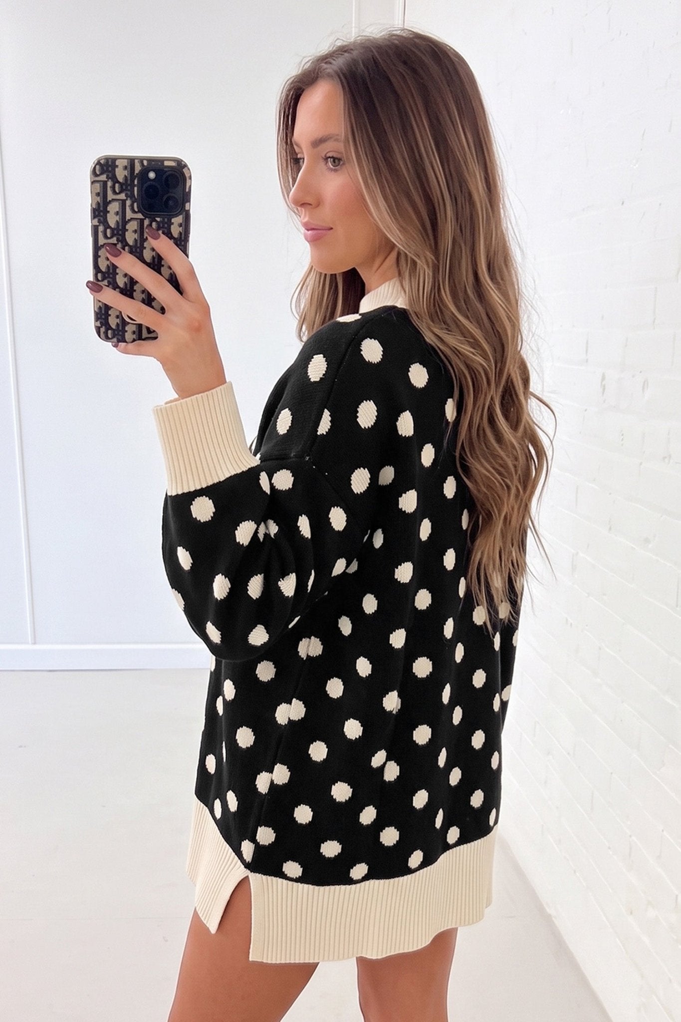 Woman in black knit sweater with cream polka dots and ribbed trim.