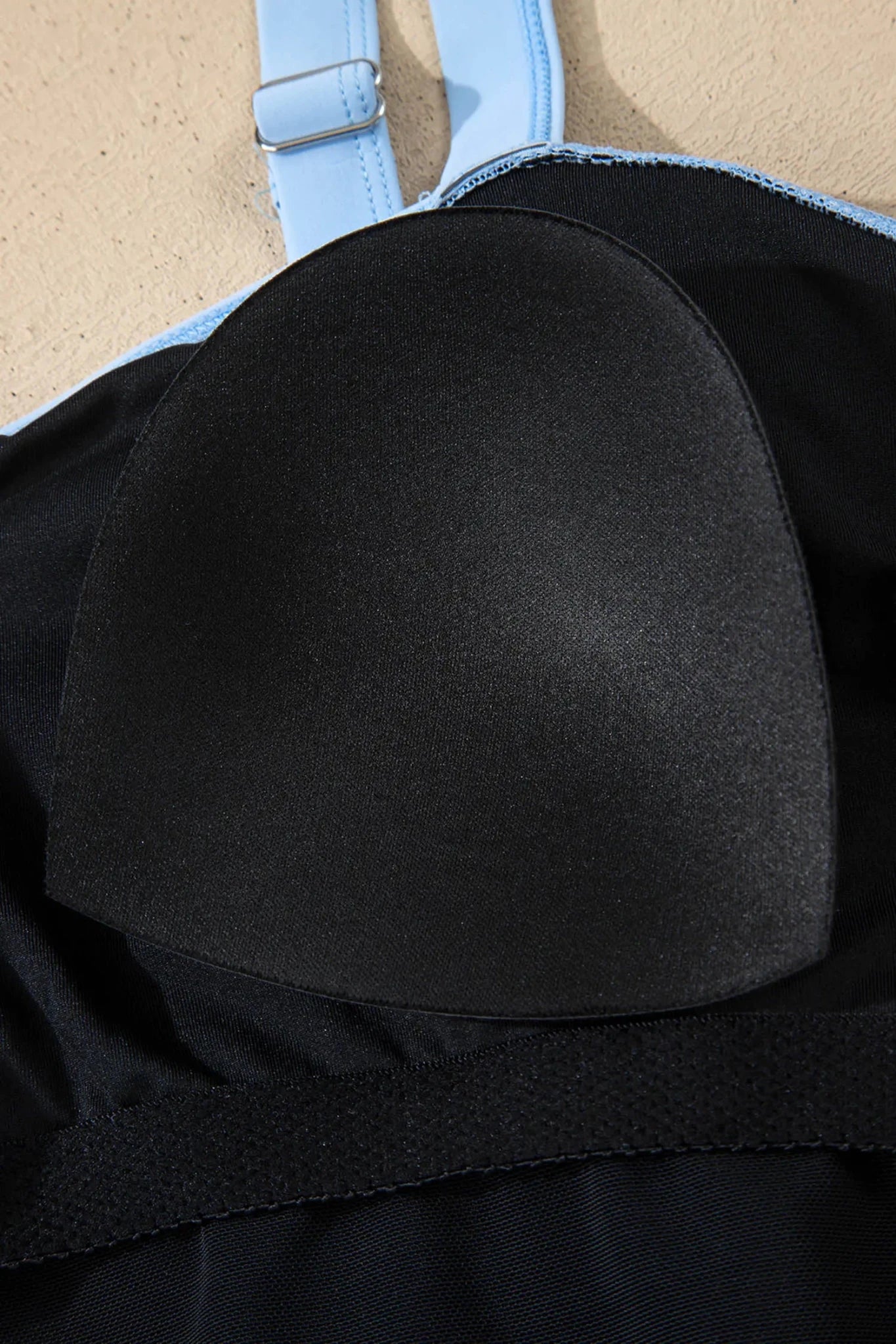 Black bikini top with blue straps on a beige background