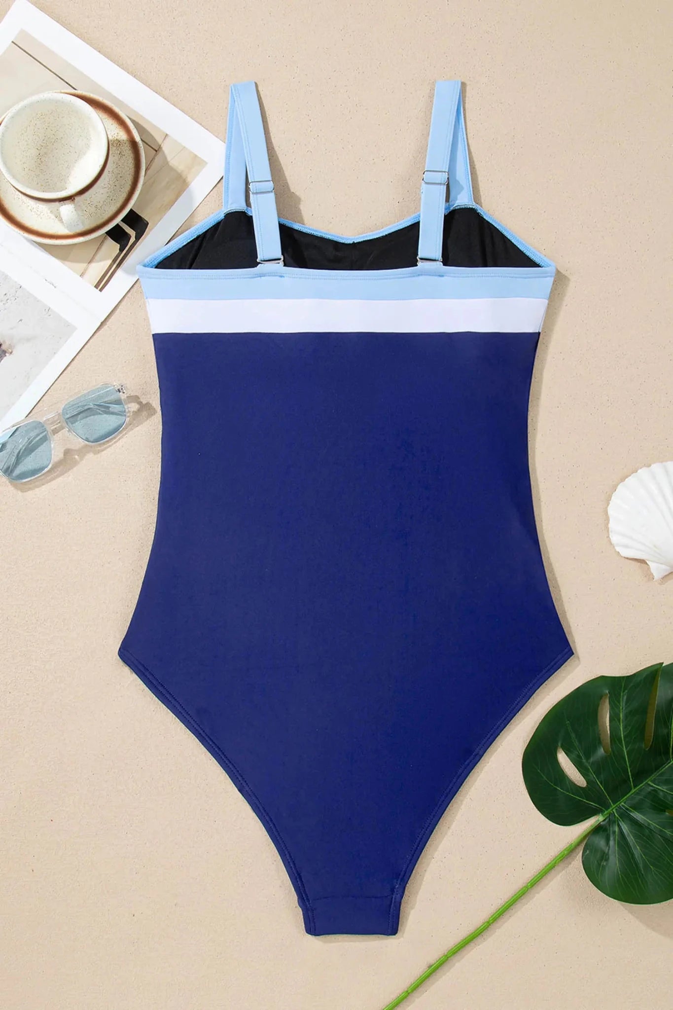 Blue and black swimsuit on a beige surface with a magazine and sunglasses.