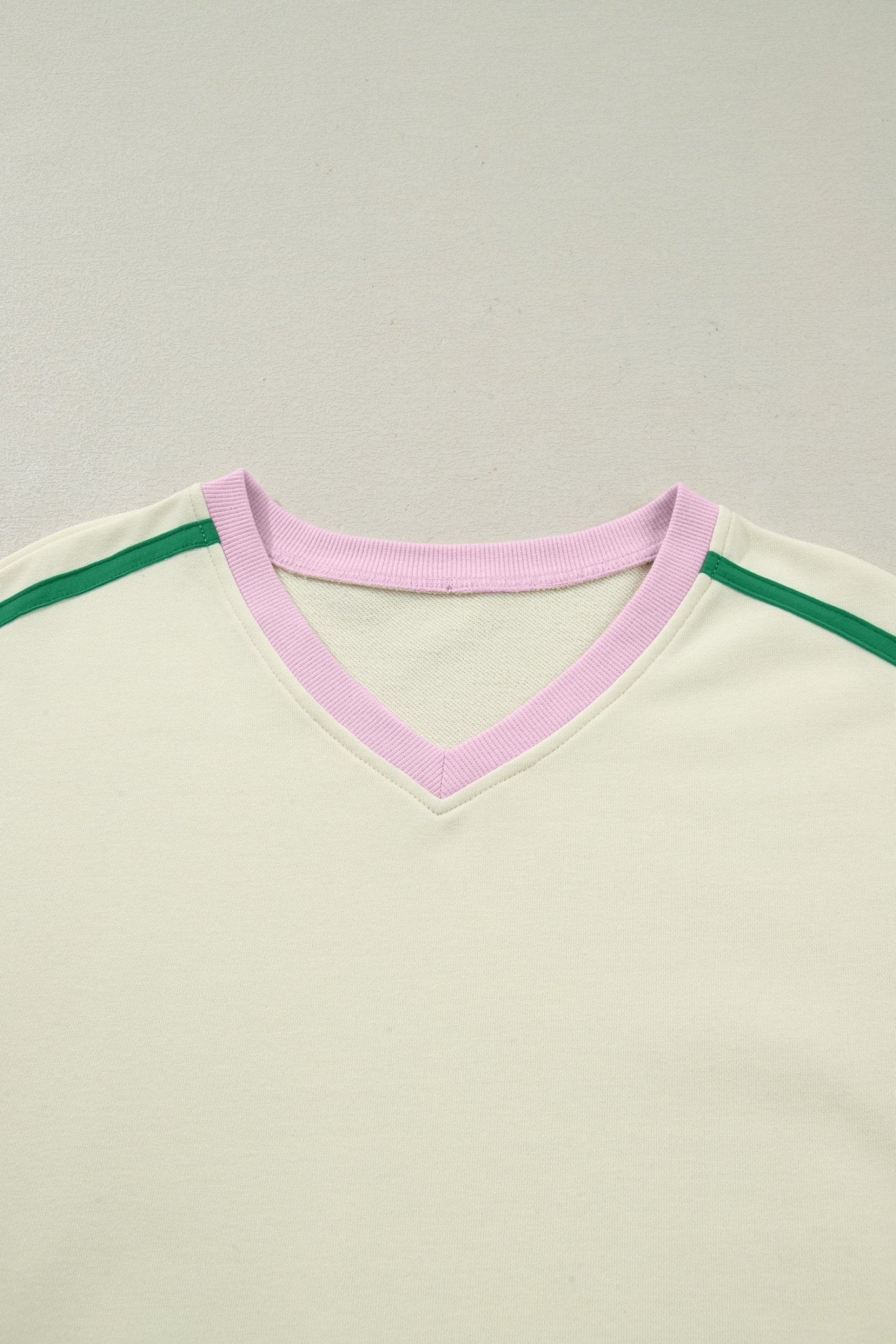 Close-up of a shirt with a pink neckline and green accents on a light gray background