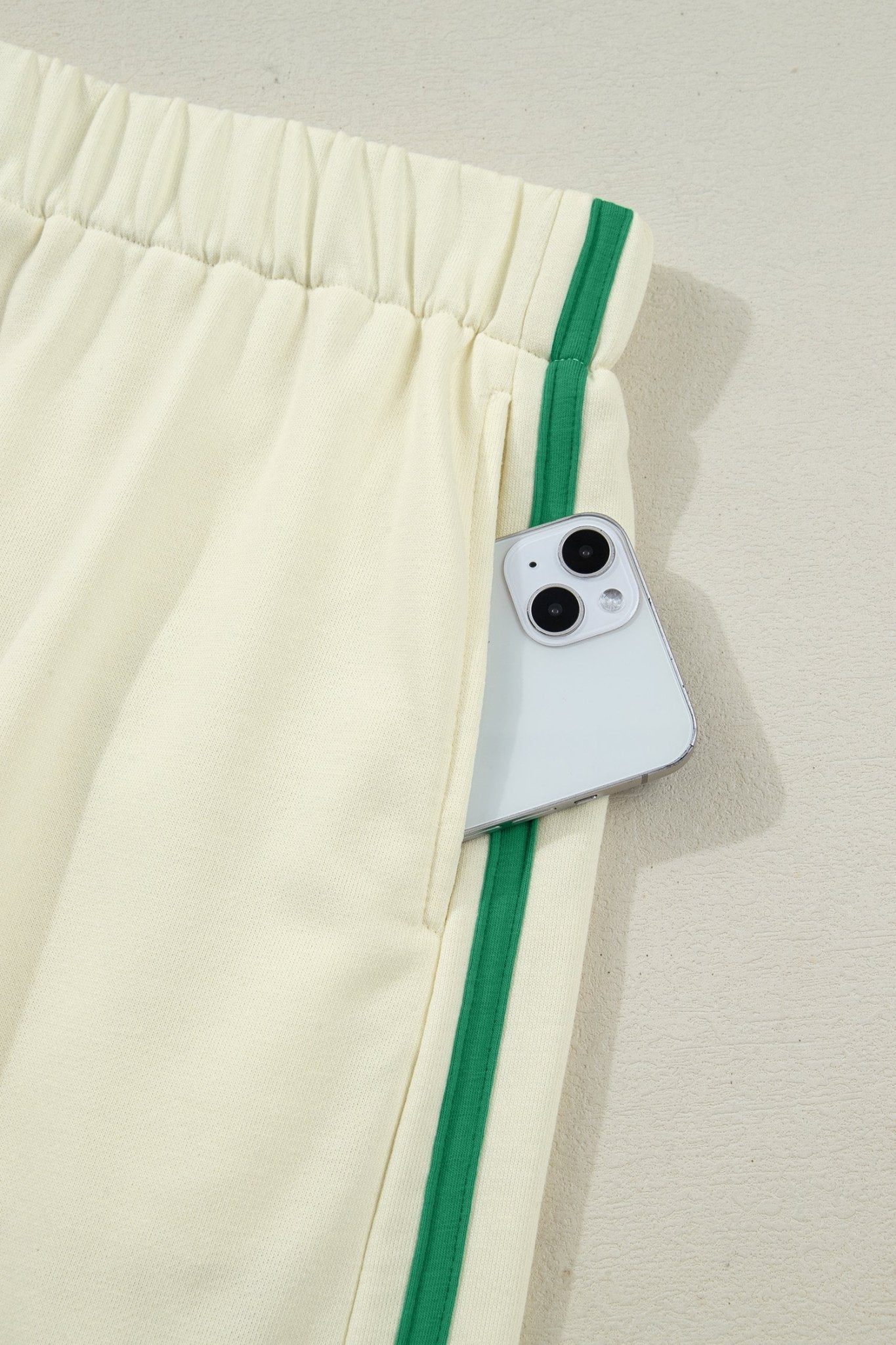 White pants with green trim and a phone case on a light gray background