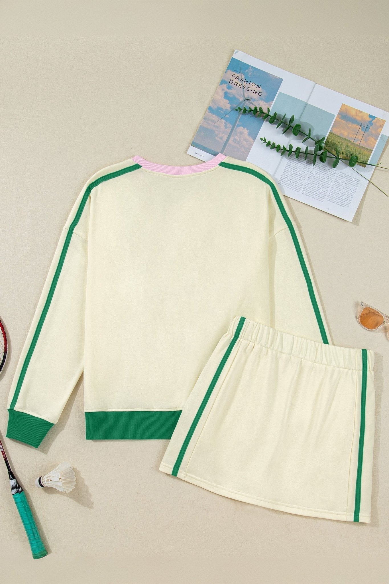 Cream-colored outfit with green accents on a beige surface with a magazine and plant.