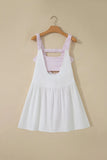 A white sleeveless pinafore-style dress with a pink and white gingham patterned underbust band and shoulder straps, hanging on a wooden hanger against a beige wall.