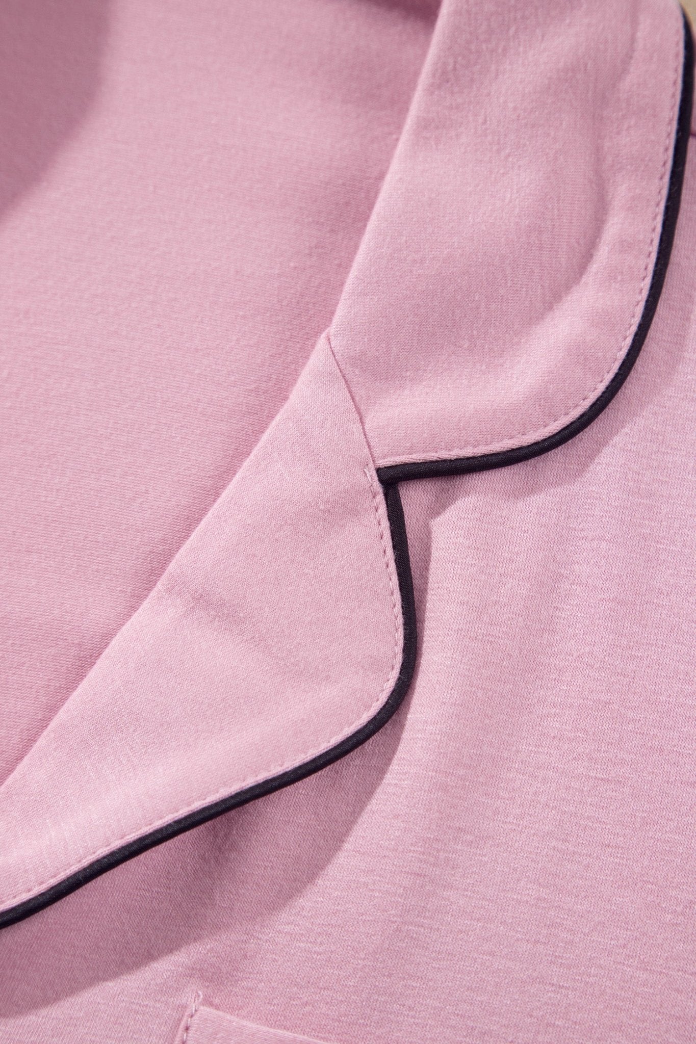 Close-up of a pink garment with black piping trim along the collar and pocket edges.