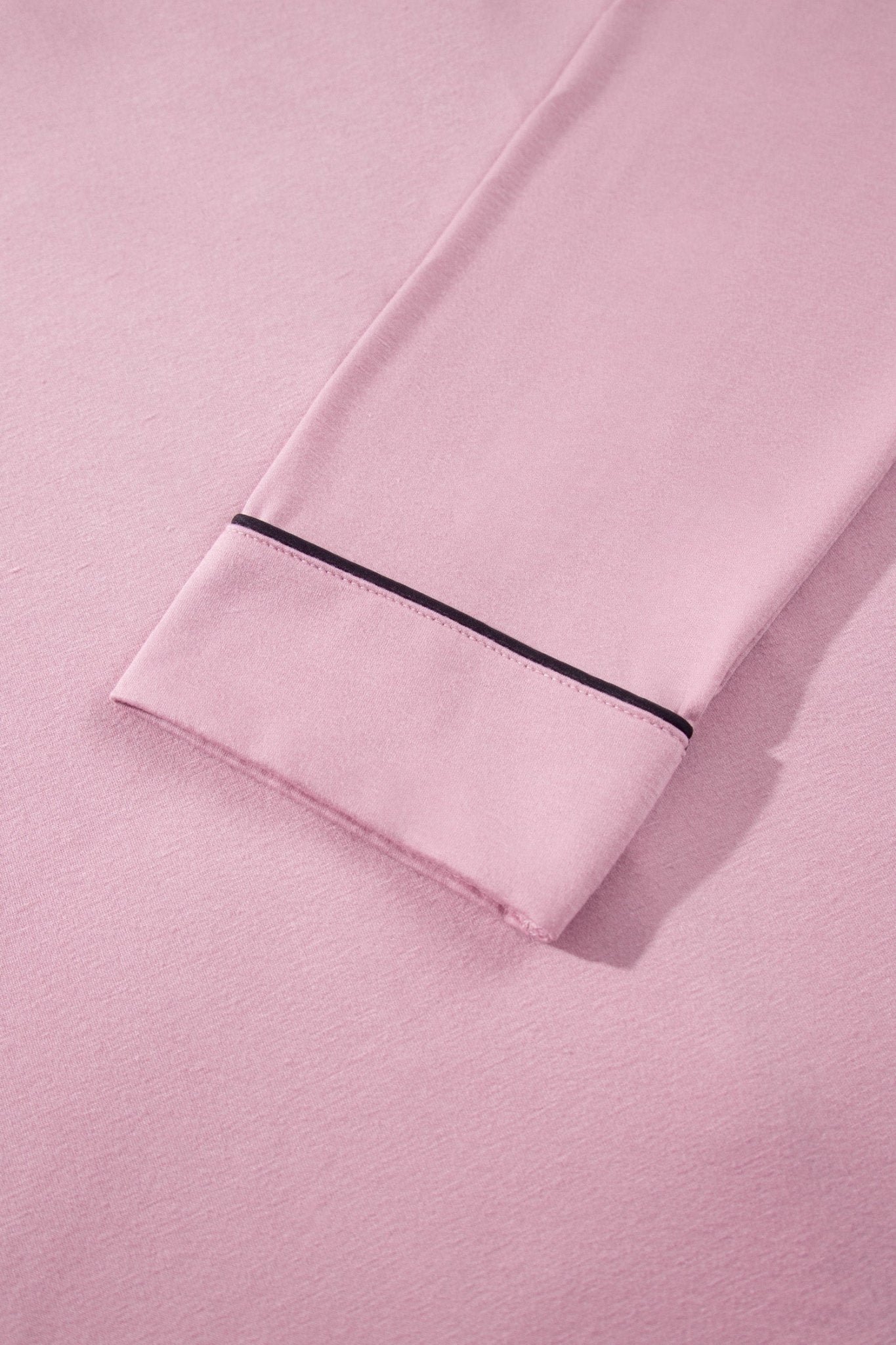 Close-up of light pink fabric with folded cuff and black piping trim.