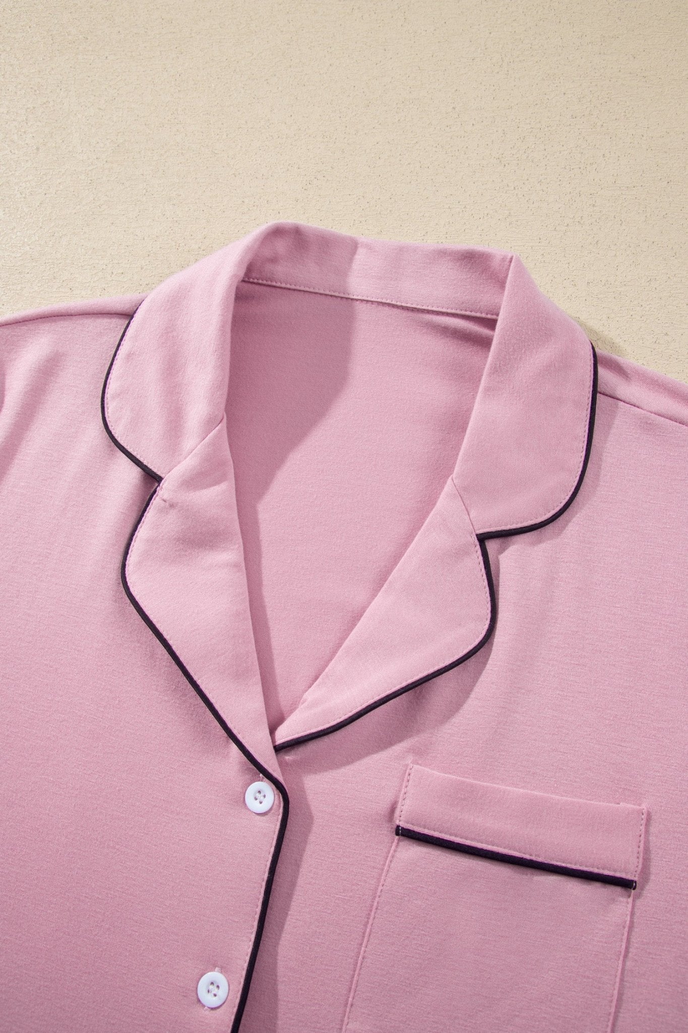 Light pink pajama garment showing a folded cuff with thin black piping on matching background