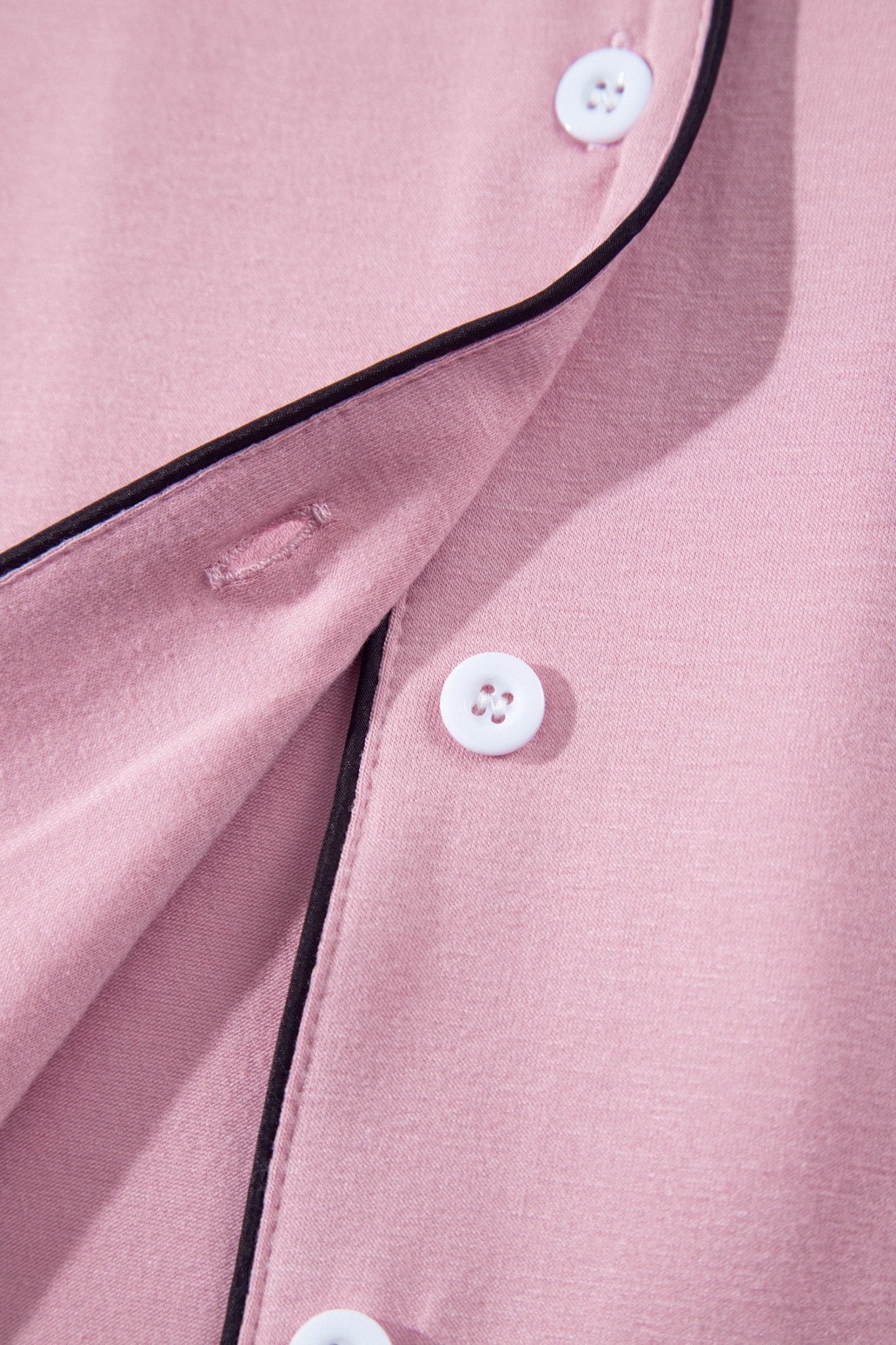 Close-up of a dusty pink button-up shirt with black piping trim and white buttons.
