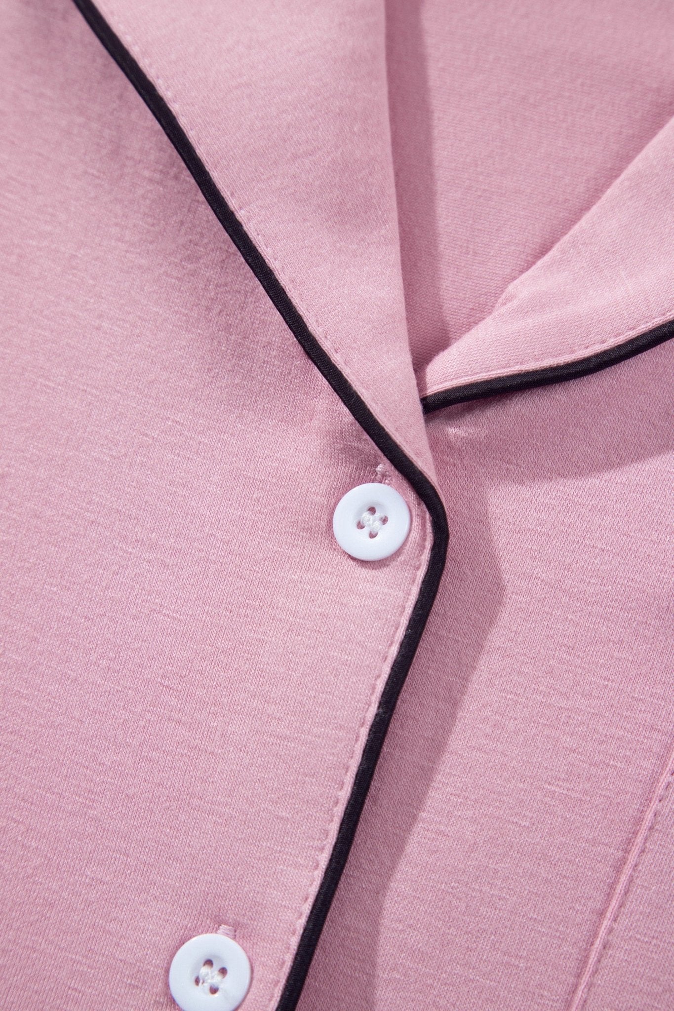 Close-up of a pink pajama shirt with black piping trim and white buttons.