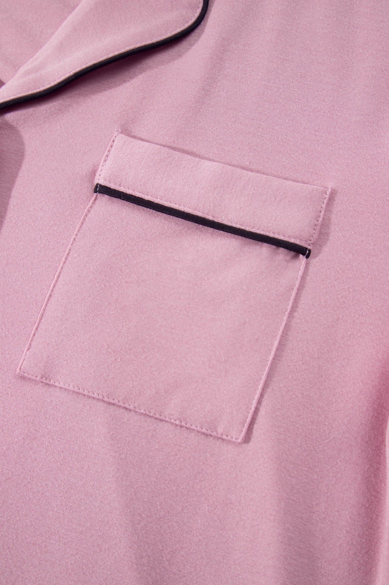 Close-up of a pink fabric garment with a chest pocket and thin black piping trim.