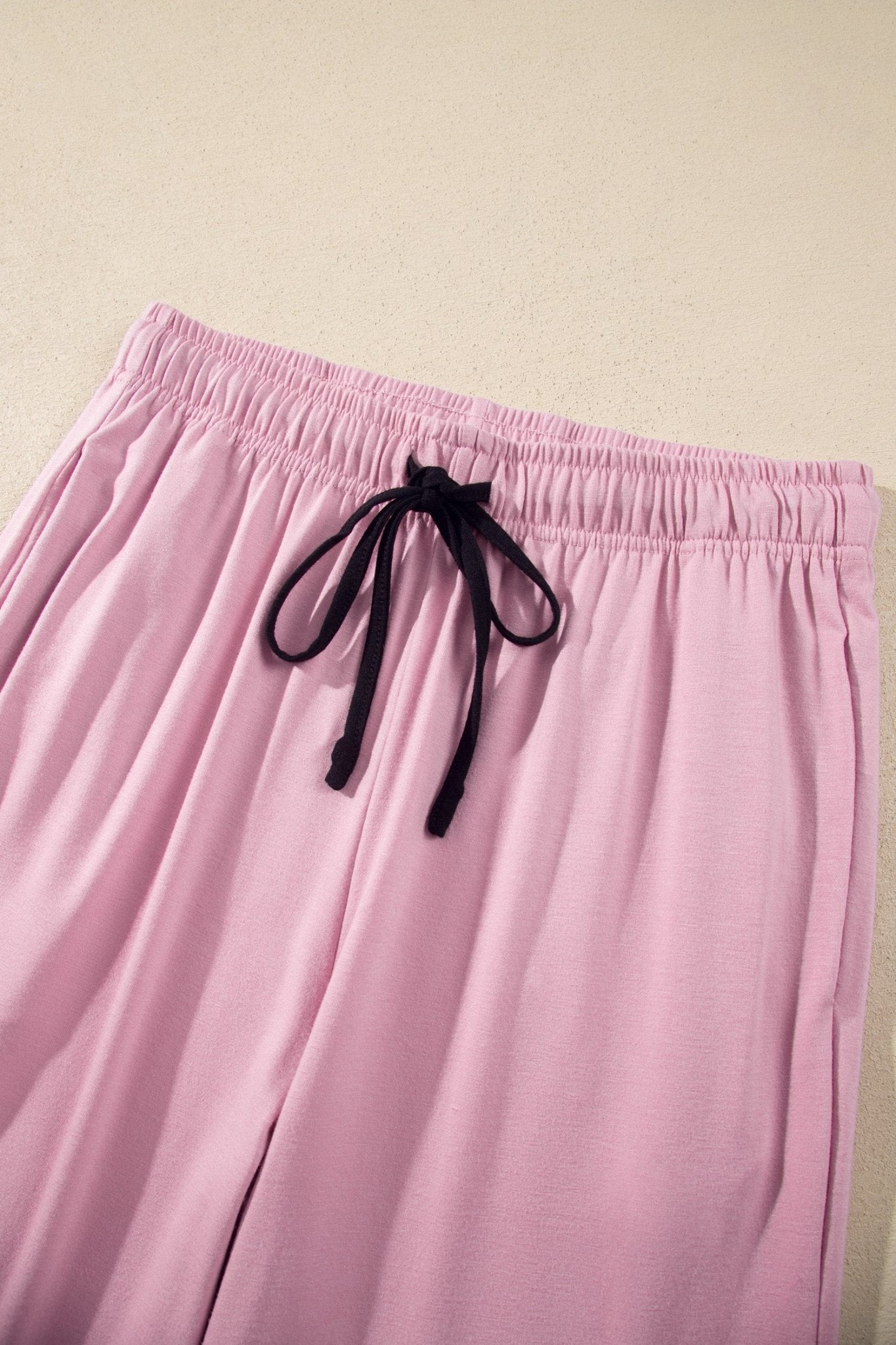 Pink lounge pants with an elastic waistband and black drawstring, shown against a plain beige background.