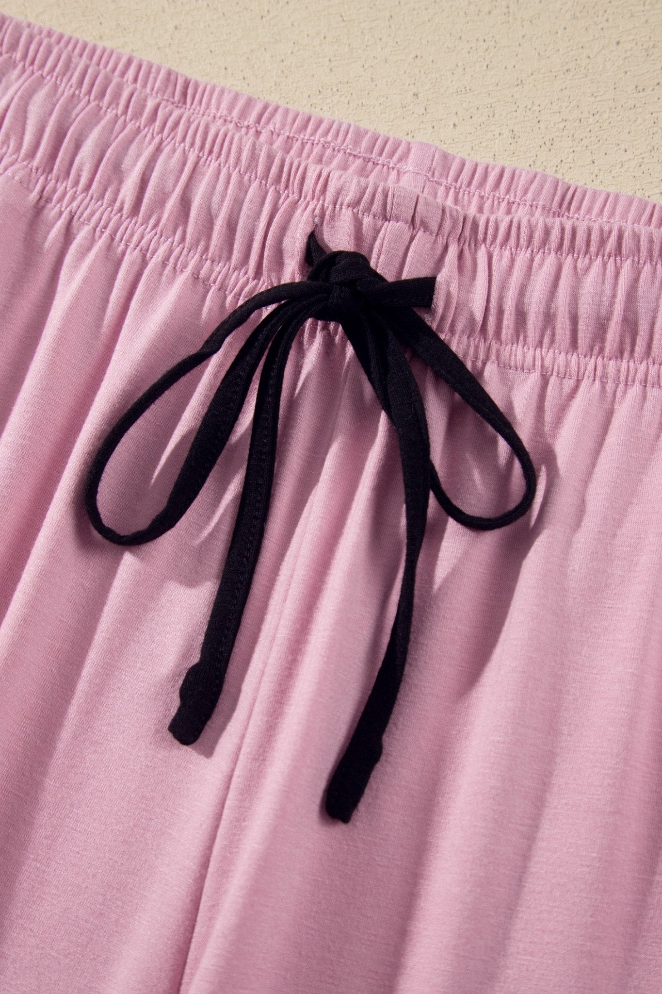 Pink pajama pants folded on beige surface, featuring thin black piping along the cuffs.