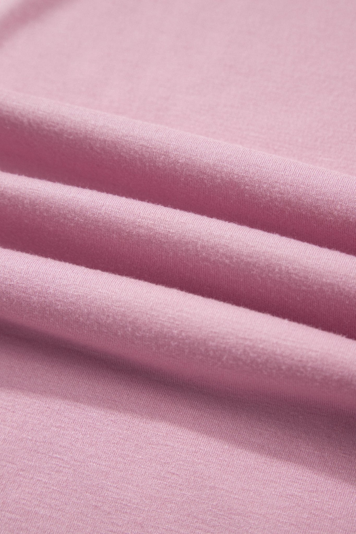 A close-up of soft pink fabric with gentle folds showing the material texture.