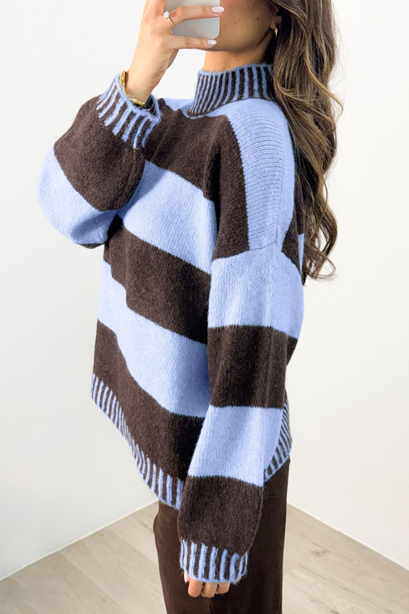 Woman in fuzzy brown-blue striped mock-neck sweater, mirror selfie in bright room.