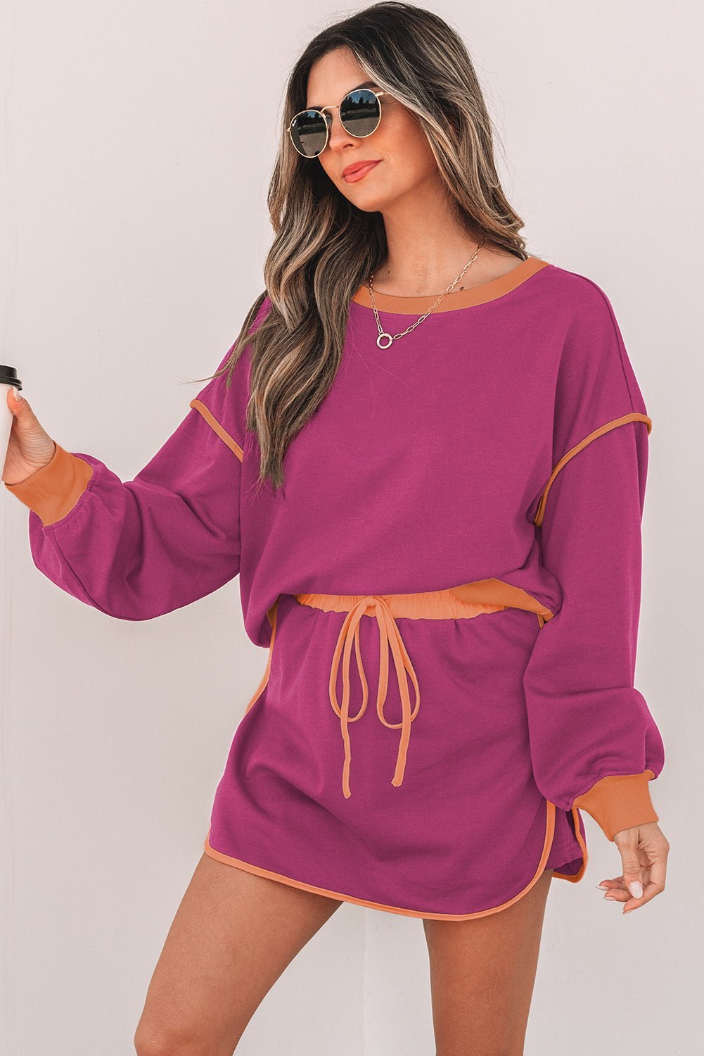 Woman wearing a purple outfit with orange accents on a plain background