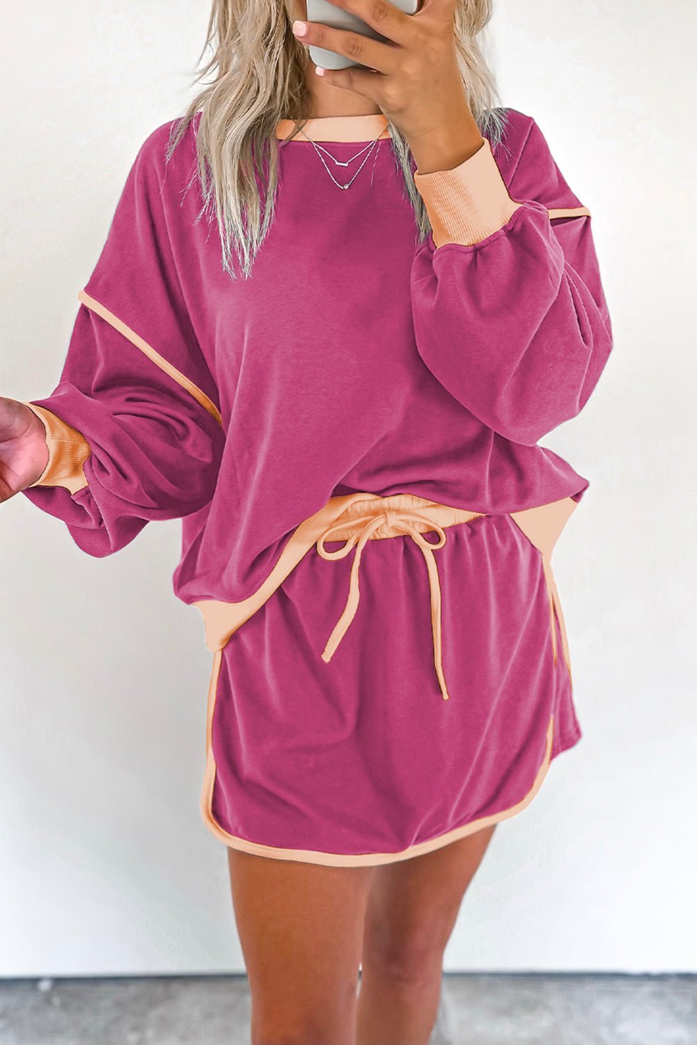 Person wearing a magenta lounge set with peach trim against a white background