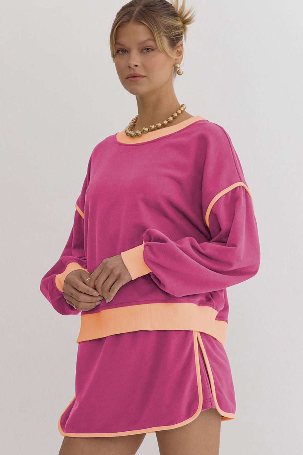 Woman wearing a pink dress with orange accents on a plain background