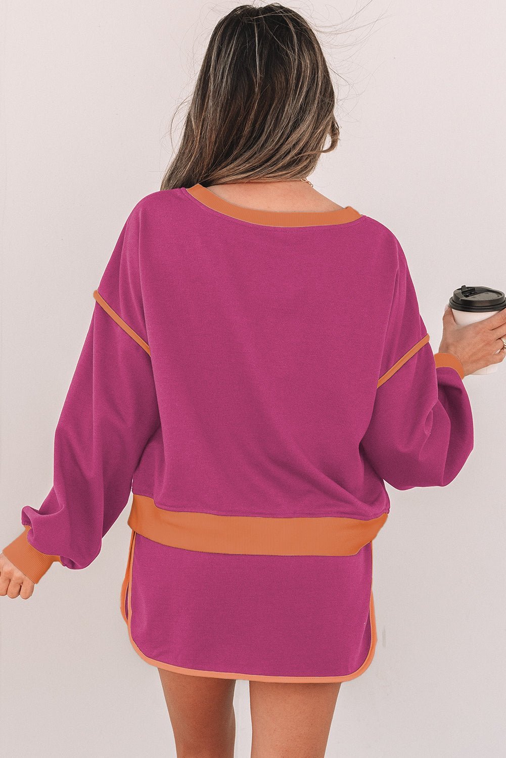 Woman wearing a purple dress with orange accents, holding a coffee cup.
