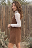 Woman in brown corduroy pinafore over a white lace long-sleeve top.