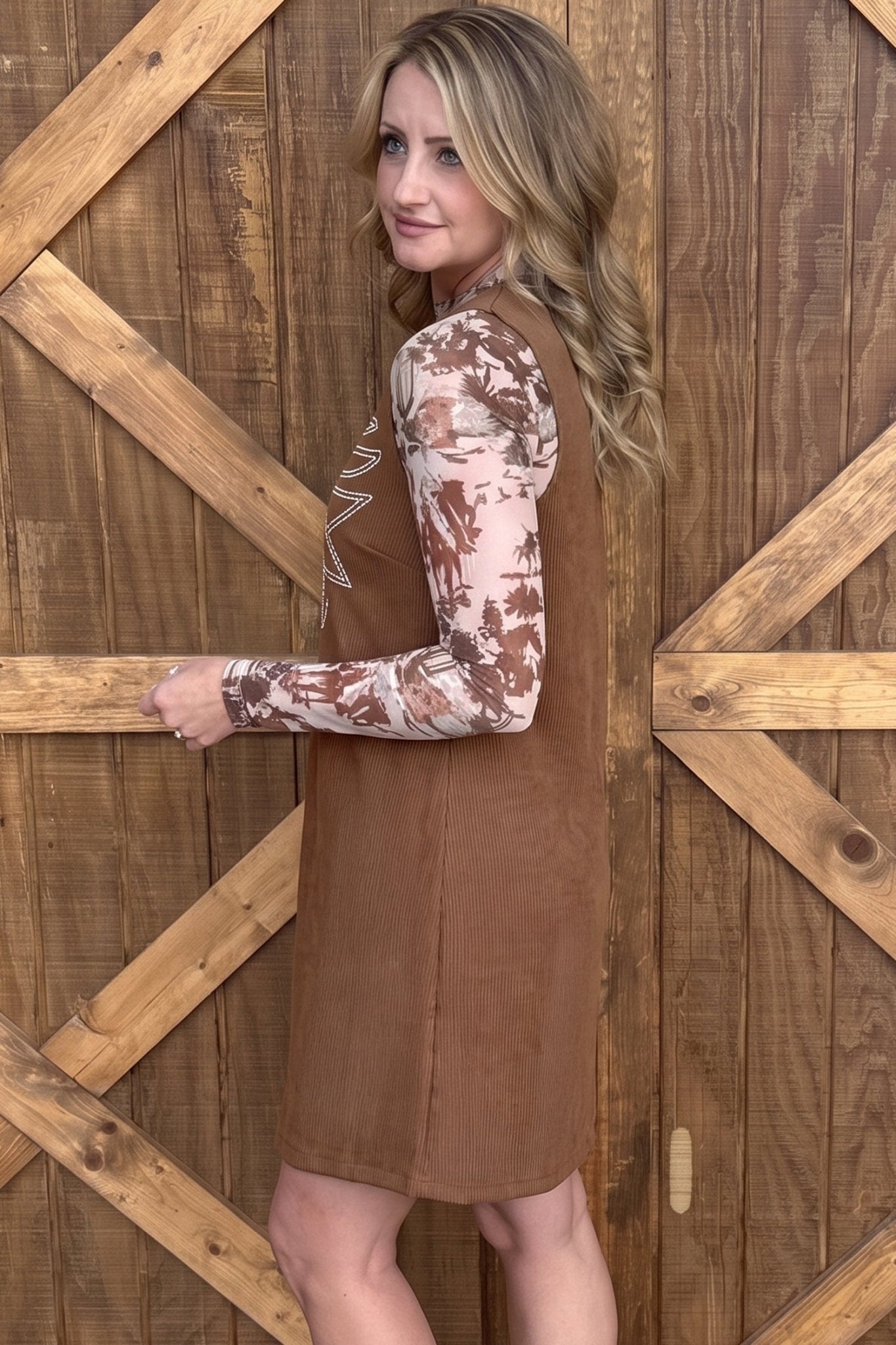 Woman in brown sleeveless dress over a floral long-sleeve top.
